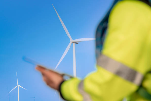 istock A blurred figure holding a tablet observes large wind turbines in the background under a clear blue sky, symbolizing renewable energy, modern technology, and sustainable environmental solutions. 2187306480