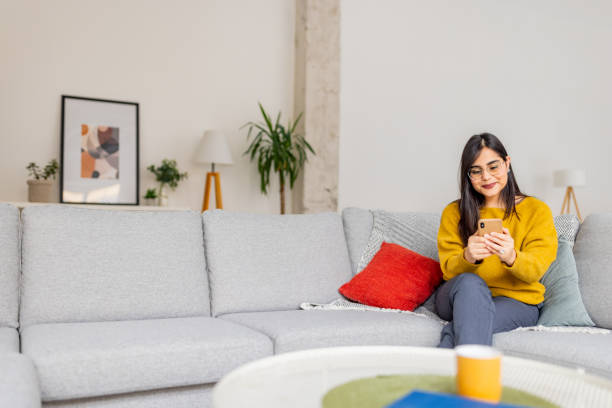 istock Young woman on sofa with smartphone in bright room 2187306927