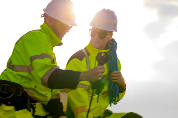 istock Two engineers wearing high visibility safety jackets and helmets measure wind speed with an anemometer and analyze data on a tablet at a renewable energy site. The cloudy sky adds depth to the scene. 2187307330