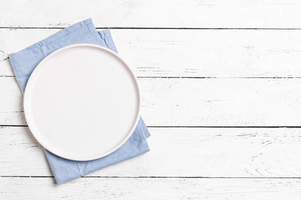 istock Empty plate and blue napkin on white wooden table 2187309376