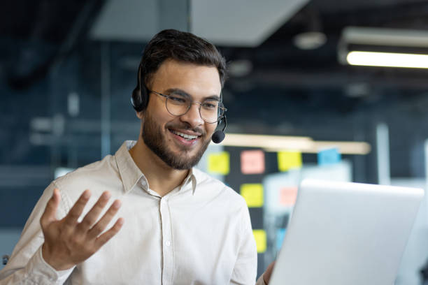 istock Confident professional in remote meeting using laptop and headset, engaging actively in an online discussion. Bright office environment enhances his cheerful and focused demeanor. 2187310375