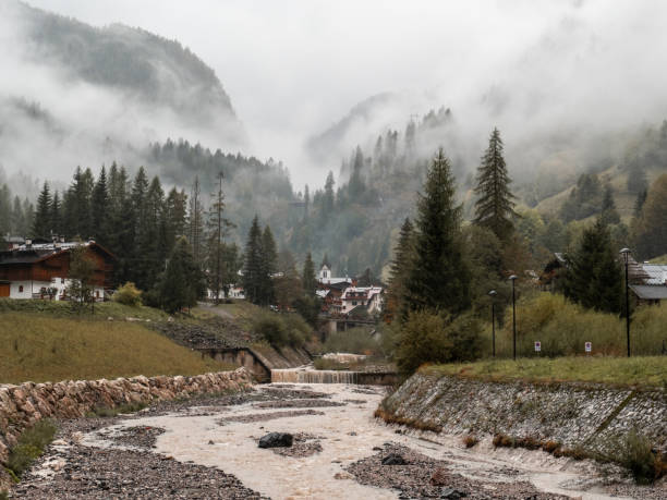 The village of Rocca Pietore appears through the mist, its peaceful atmosphere contrasted by the majestic, forest-draped mountains looming in the distance