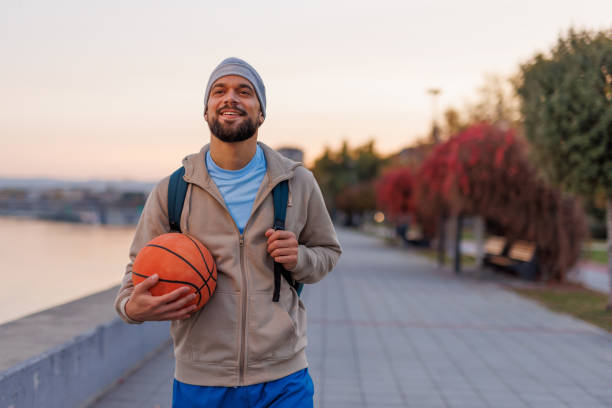 istock Contented man with basketball strolling at riverside promenade 2187312912