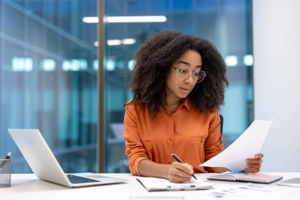 istock Focused professional woman working at modern office desk with laptop and documents in bright corporate environment. 2187313373