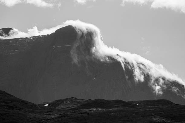 Black and white landscape of cloudy mountaintops, clouds rolling and falling over mountain edge