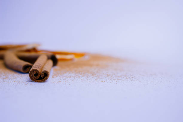 A pile of orange slices and cinnamon sticks on a white background. The oranges are cut in half and the cinnamon sticks are whole. Concept of warmth and comfort