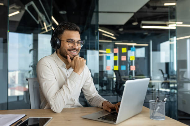istock Smiling professional man in headphones working remotely on laptop during video call from modern office 2187314276
