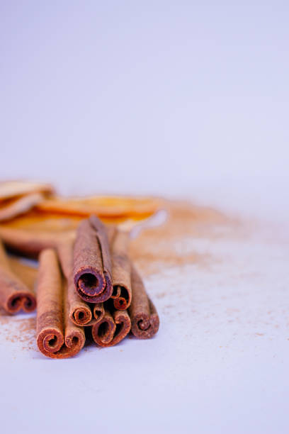 A pile of orange slices and cinnamon sticks on a white background. The oranges are cut in half and the cinnamon sticks are whole. Concept of warmth and comfort