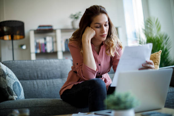istock Young woman analyzing financial documents while working on her laptop at home 2187314456
