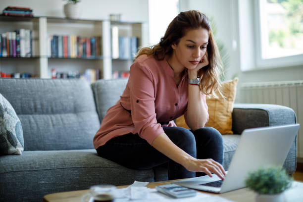 istock Young woman analyzing financial documents while working on her laptop at home 2187314471