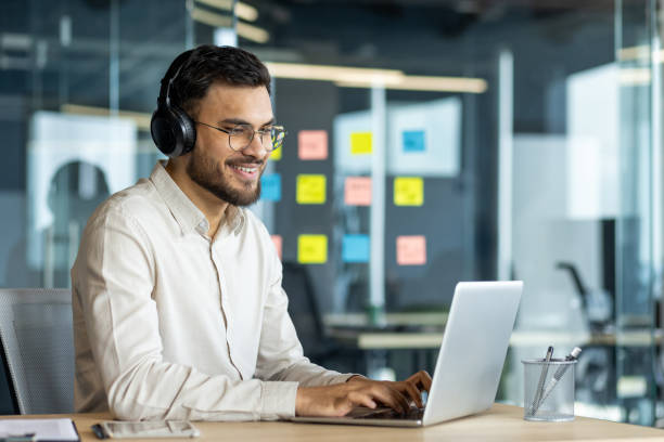 istock Smiling man wearing headphones working on laptop in modern office setting focused on task 2187314932