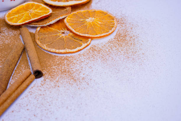 A pile of orange slices and cinnamon sticks on a white background. The oranges are cut in half and the cinnamon sticks are whole. Concept of warmth and comfort