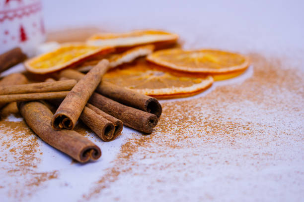 A pile of orange slices and cinnamon sticks on a white background. The oranges are cut in half and the cinnamon sticks are whole. Concept of warmth and comfort