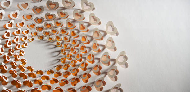 Intricate cut paper artwork featuring layered heart shapes arranged in a circular pattern with gentle shadows. The design evokes romantic and Valentine themes, offering a modern and elegant aesthetic perfect for love-inspired projects or decorations.\nNative image size: 10875 x 5304.