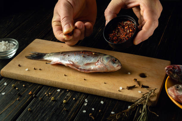 istock Hands skillfully sprinkle spices over a freshly caught fish laid on a wooden cutting board. Nearby, salt crystals shimmer, adding to the flavorful preparation on a rustic table. 2187321927