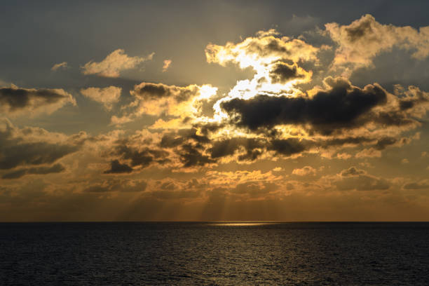 At Sea - December 31, 2017: The sun sets behind dramatic clouds, casting golden rays over the tranquil ocean.