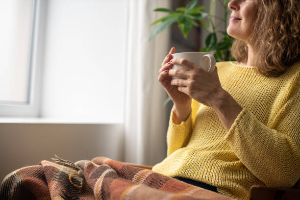 Tranquil woman with a mug sitting under warm blanket
