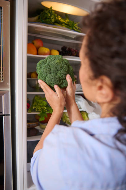 istock Woman holding fresh broccoli in a well-stocked refrigerator 2187327748
