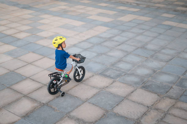 The image features a young cyclist enjoying a leisurely ride across a spacious, tiled outdoor area, secured with a yellow helmet, signifying freedom and enjoyment.