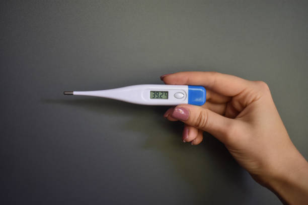 istock Female hand with electronic thermometer on dark background 2187336688