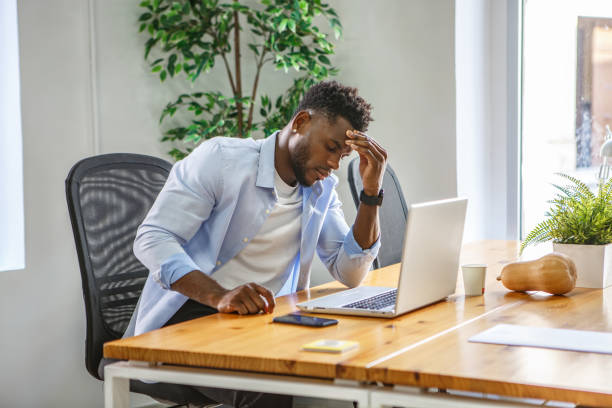 istock A worried man sits at his office desk while working on his laptop in a bright, modern workspace 2187338188