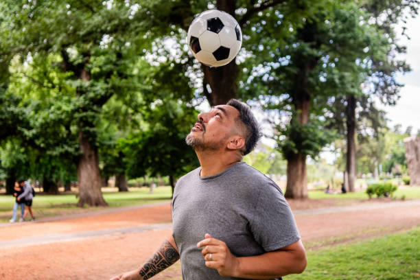 Mature man doing keep ups with soccer ball on the public park