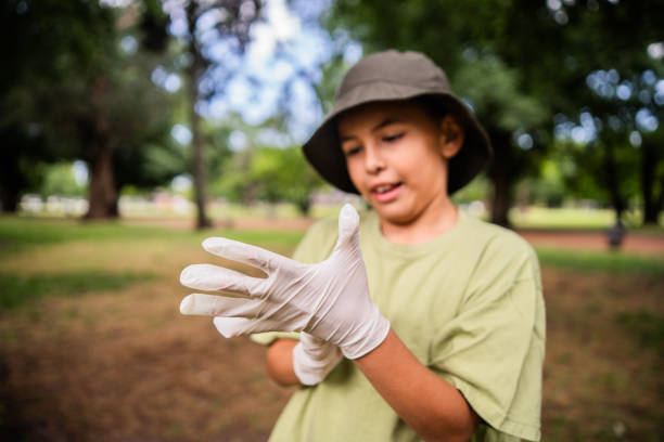 Child boy wearing gloves before collecting trash in a public park