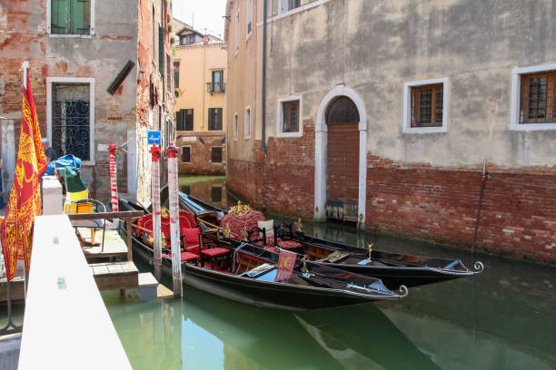 Side view of two empty black wooden traditional gondola boat standing moored on narrow water canal on city street in downtown district in a sunny summer day in Venice, Italy. Travel in Europe theme.