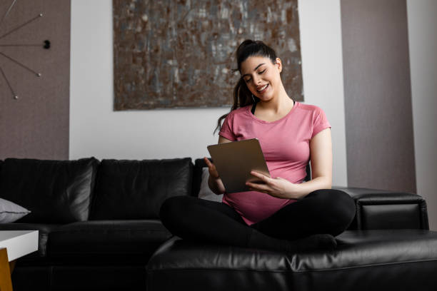 istock Pregnant woman using digital tablet and sitting on sofa at living room 2187339996