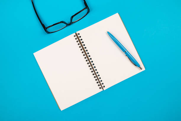 istock Top view of white blank notepad with pencil and glasses on isolated blue background with copy space. 2187340615