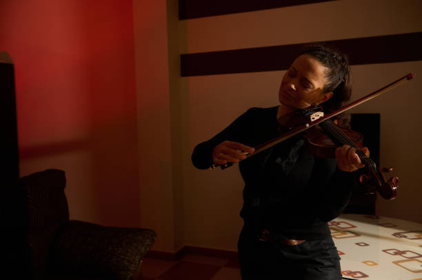 istock Woman playing violin with joyful expression in dimly lit room 2187344933