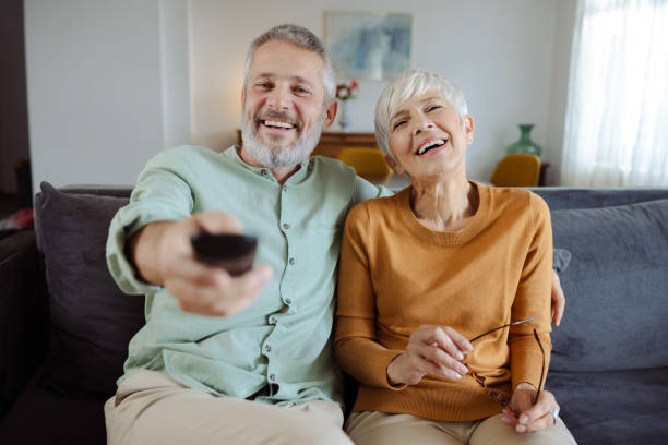 istock Joyful seniors laughing while watching TV together at home 2187345579
