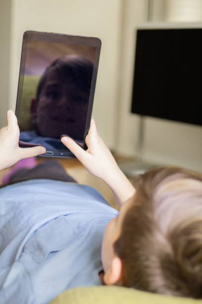 istock Teenage boy is using e-reader to reading e-book on the floor at home. He is studying for school test. Technology and education. 2187347184