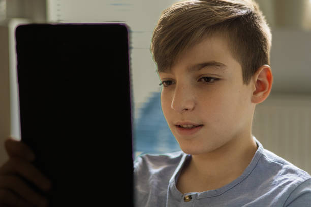 istock Teenage boy is using e-reader to reading e-book at home. He is studying for school test. Technology and education. 2187347500