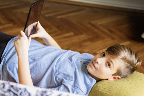 istock Teenage boy is using e-reader to reading e-book on the floor at home. He is studying for school test. Technology and education. 2187347766