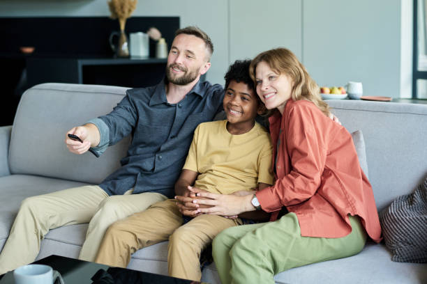istock Smiling Family Sitting on Sofa and Watching TV Together 2187351202