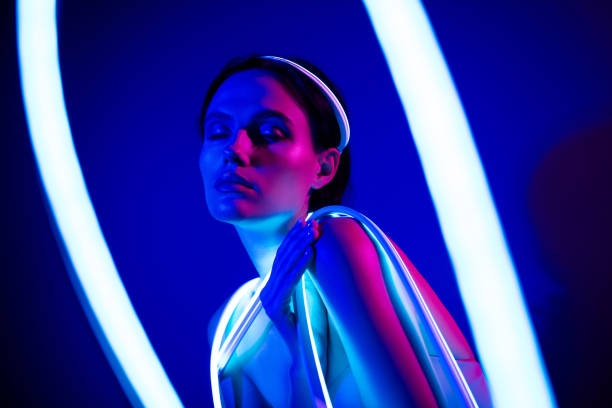 istock Elegant young model posing under vibrant neon blue lights in a futuristic studio setting 2187352175
