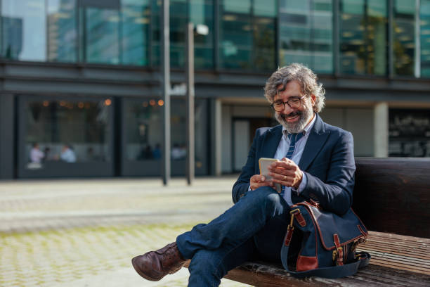 istock Smiling businessman using smartphone on bench outside office 2187353047