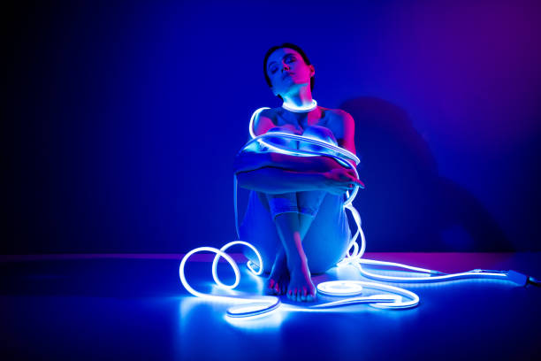 istock Young woman enveloped in neon lights posing elegantly against a dark blue background in a studio setting 2187353242