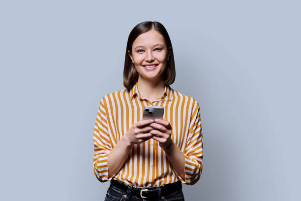 istock Young smiling woman using smartphone looking at camera in grey background 2187355985