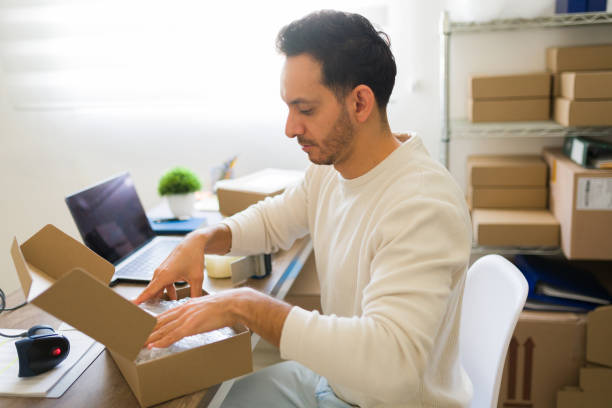 istock Small business owner carefully packing products into cardboard box, preparing orders for shipment in his home office 2187360623