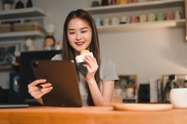 istock Enjoying snack while using tablet, young woman smiles in cozy indoor setting. warm atmosphere highlights her relaxed demeanor and engagement with device 2187363644