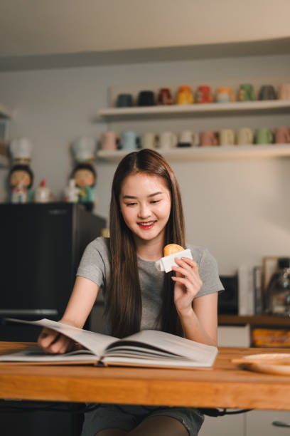 istock Enjoying delicious pastry while reading book, young woman smiles in cozy kitchen setting. warm atmosphere enhances her joyful experience 2187363673