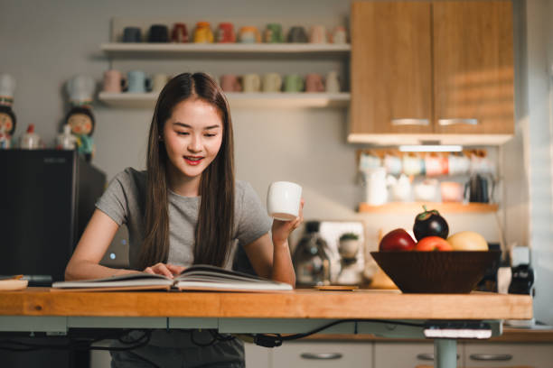 istock young woman enjoys quiet moment reading book while holding cup in cozy kitchen. warm lighting and colorful mugs in background create welcoming atmosphere 2187363685