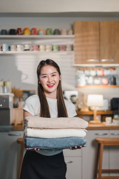 istock young woman smiles while holding stack of neatly folded towels in cozy kitchen setting. warm ambiance and her cheerful expression create welcoming atmosphere 2187364496