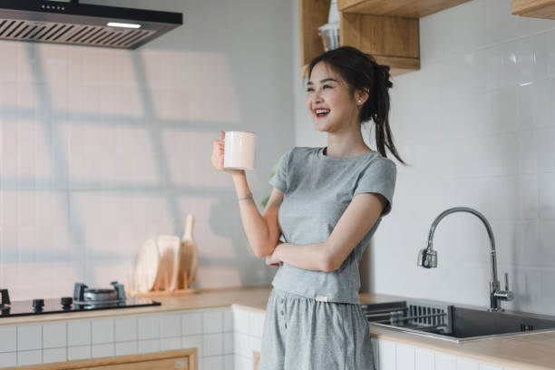 istock woman in gray outfit smiles joyfully while holding pink mug in modern kitchen. sunlight casts soft shadows, enhancing cheerful atmosphere of space 2187364549