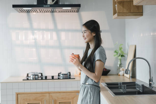istock young woman stands in modern kitchen, holding cup and smiling. bright space features sleek cabinetry and stylish sink, creating warm and inviting atmosphere 2187364578