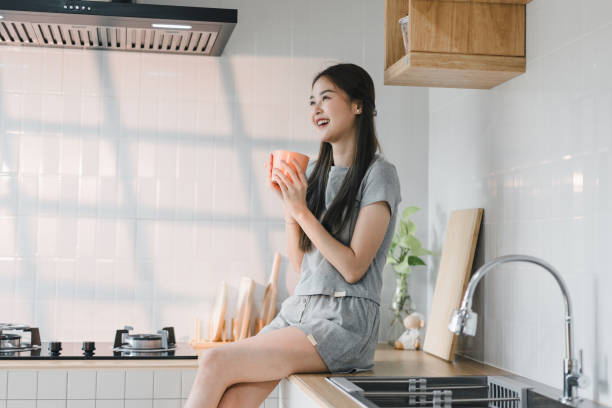 istock young woman sits on kitchen counter, enjoying warm drink in cozy, modern kitchen. sunlight streams through window, creating cheerful and inviting atmosphere 2187364583