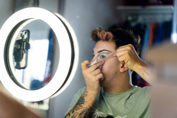 Drag queen applying makeup in front of a ring light with smartphone