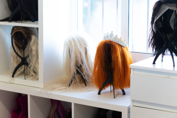 Colorful wigs and a tiara resting on a white shelf in a dressing room